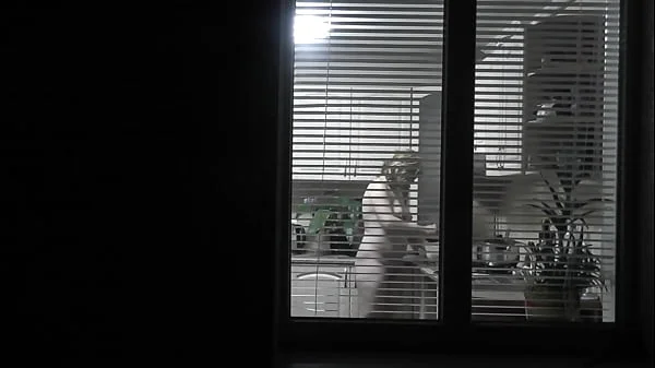 Peeping. Voyeur. Neighbor pervert voyeur in evening on street looks out window as naked sexy neighbor in kitchen prepares dinner for her husband. Naked in public. Naked at home. Family.  Outdoor